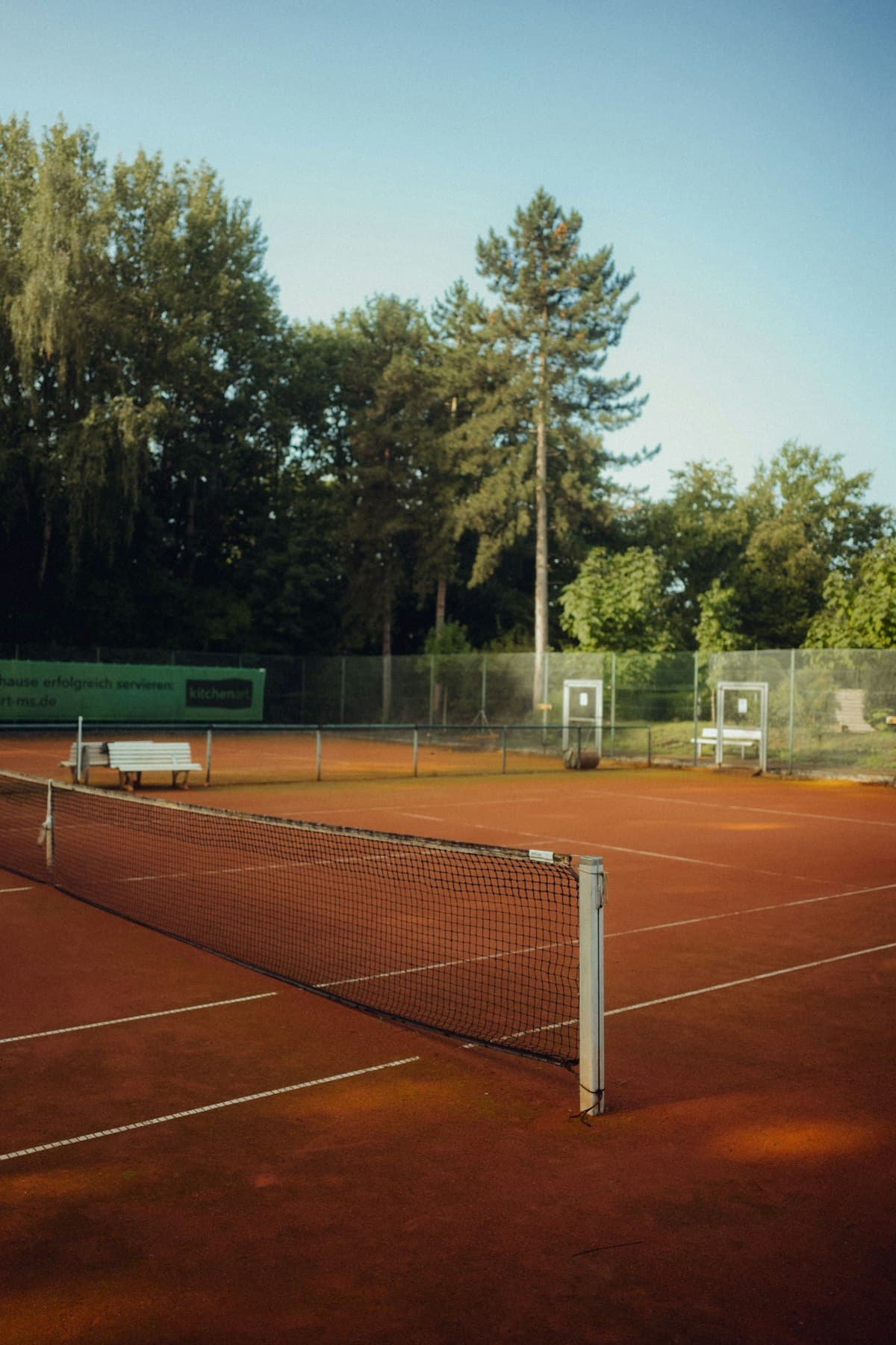 An empty clay tennis court surrounded by trees